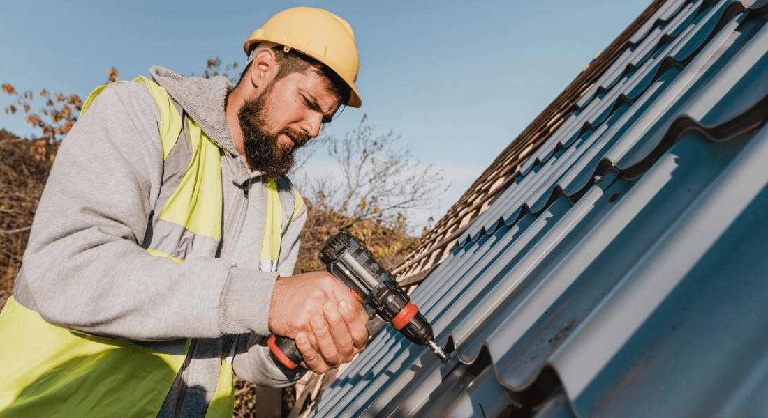written by:, sideways man working roof with drill