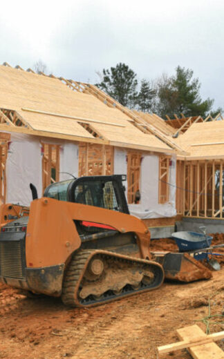 Construction site with heavy machinery, including a skid steer loader, working on a new residential building project."